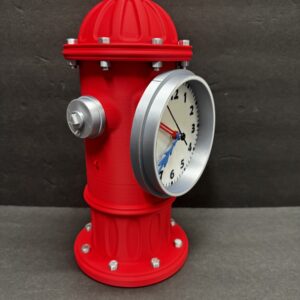 Red fire-hydrant shaped tabletop clock with a silver-rimmed white clock face mounted on the side, black numerals, a blue minute hand and red second hand, and silver bolts against a dark gray background.