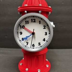 Red fire-hydrant-shaped tabletop clock with a white dial, bold black numerals, a silver bezel and visible bolts, a short red hour hand, a blue decorative minute hand and a thin black second hand against a dark gray background.