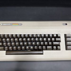 Top-down view of a beige Commodore 64 computer chassis and keyboard with dark brown keycaps, a rainbow "commodore 64" logo on the upper left, a column of grey function keys on the right, and a red power LED near the top edge.