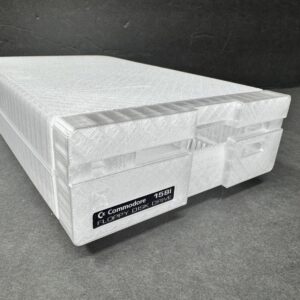 Translucent white 3D-printed replica of a Commodore 1581 floppy disk drive angled on a dark gray surface, showing the front drive slot, Commodore label and visible print-layer texture.