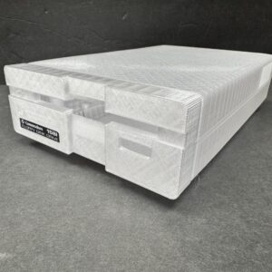 White 3D-printed replica of a Commodore 1581 floppy disk drive with visible layer texture, placed on a dark gray surface against a black background.
