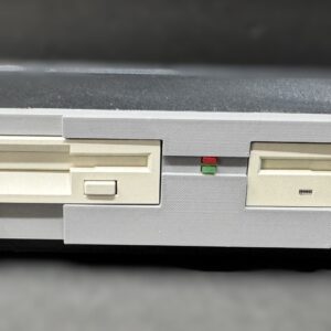 Front view of a grey Commodore 1581 floppy disk drive with two beige disk slots, small red and green LED indicator lights, and a red Commodore 1581 floppy disk drive badge on the lower left.