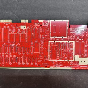 Red printed circuit board (Commodore 64 replica) laid flat on a dark background, with white silkscreen outlines, many unpopulated through‑hole component footprints, edge connectors and printed labels.
