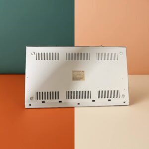 Beige Commodore 64 bottom panel with multiple ventilation slots and a central label, set against a four-quadrant teal, peach, orange, and cream background.