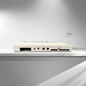 Beige vintage computer keyboard photographed from the rear on a white shelf, showing a wide connector slot, two round DIN ports and dual card slots against a minimal light-gray wall with soft shadows.