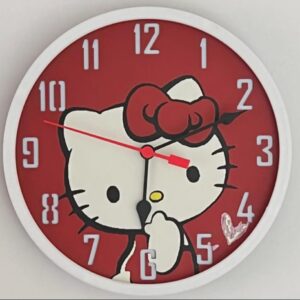 Round wall clock with a white frame and red face featuring a large Hello Kitty illustration wearing a red bow, pale gray Arabic numerals around the dial, black hour and minute hands and a thin red second hand, and a small heart sticker near the 4 o'clock position.