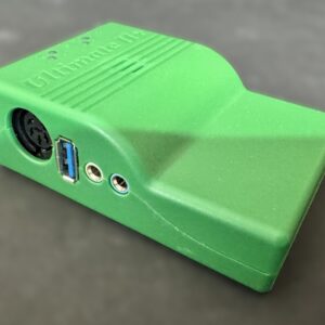 Bright green plastic electronic adapter enclosure with a round DIN connector, a blue USB 3.0 B port and two 3.5 mm audio jacks, shown angled on a dark surface.